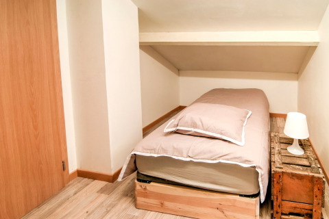 Small bedroom at «Au Coeur du Pêcheur» in Belgium, single bed, rustic wood nightstand, and lamp.
