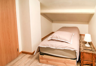 Small bedroom at «Au Coeur du Pêcheur» in Belgium, single bed, rustic wood nightstand, and lamp.