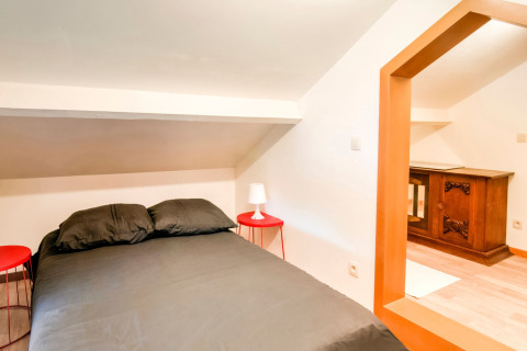 Bedroom with black bedding, sloped ceiling, two red nightstands and wooden cabinet at a Belgian lodge.