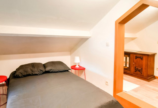 Bedroom with black bedding, sloped ceiling, two red nightstands and wooden cabinet at a Belgian lodge.
