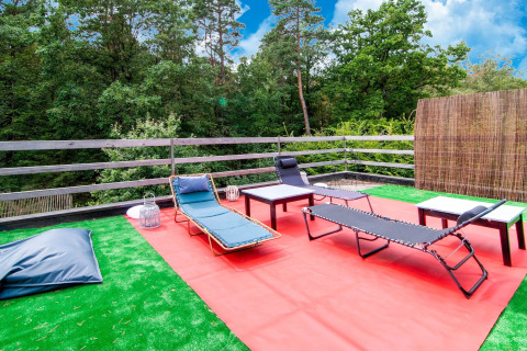 Outdoor terrace with lounge chairs and tables on artificial grass at Au Coeur du Pêcheur lodge in Belgium.