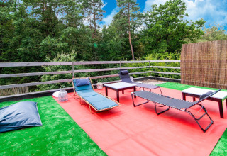 Outdoor terrace with lounge chairs and tables on artificial grass at Au Coeur du Pêcheur lodge in Belgium.