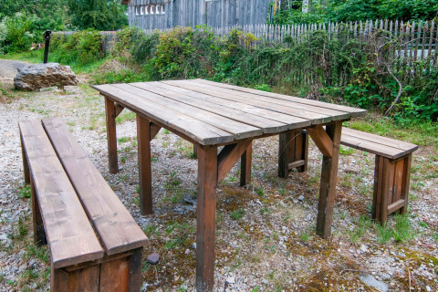 Outdoor wooden table and benches at «Au Coeur du Pêcheur» lodge in Belgium, surrounded by greenery.