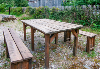 Outdoor wooden table and benches at «Au Coeur du Pêcheur» lodge in Belgium, surrounded by greenery.