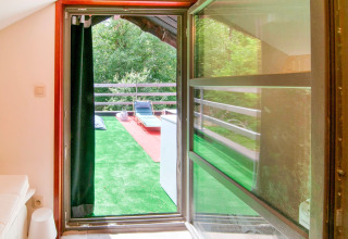 View from a room to a terrace with artificial grass and loungers at Au Coeur du Pêcheur lodge, Belgium.