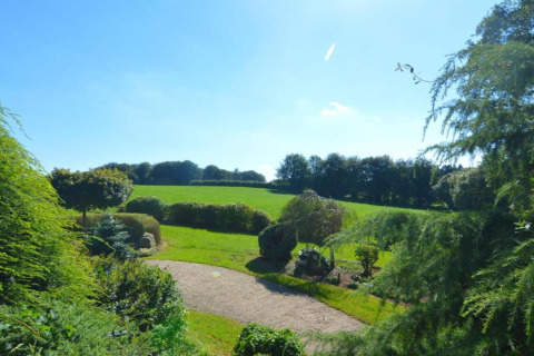 View of green fields and garden at 'Au Coeur du Pêcheur' lodge on a sunny day in Belgium.