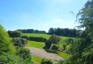View of green fields and garden at 'Au Coeur du Pêcheur' lodge on a sunny day in Belgium.