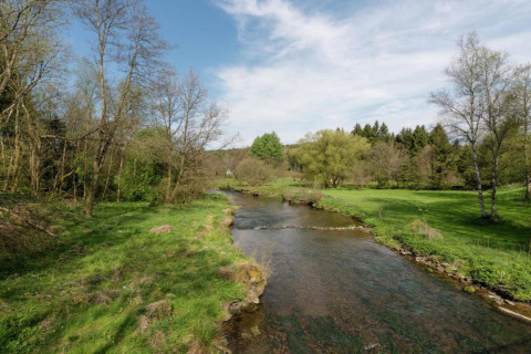 A peaceful river flows through lush green scenery at a glamping accommodation under a blue sky.