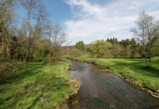 Een rustige rivier stroomt door groene natuur bij een glamping-accommodatie onder een blauwe lucht.