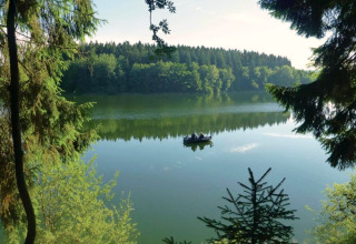 Vue sur un lac calme avec un bateau, entouré de forêt, depuis un hébergement glamping en pleine nature.