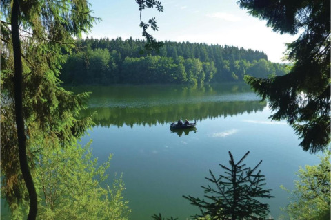 View of a peaceful lake with a boat and surrounding forest, seen from a glamping accommodation in nature.