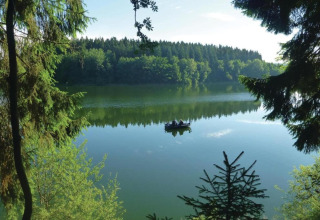 Uitzicht op een rustige meer met een boot en omringend bos, gezien vanaf een glampingaccommodatie in de natuur.