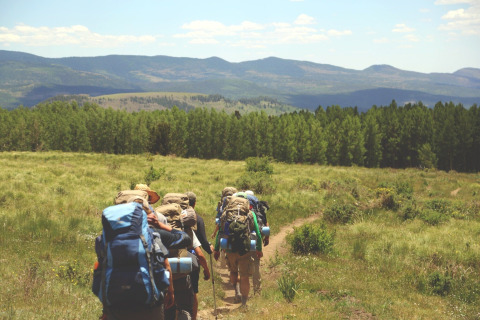 A group of hikers with backpacks treks along a scenic trail near 'Au Coeur du Pêcheur' lodge in Belgium.