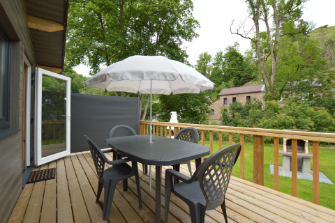 Terrasse im Le Chalet Chaleureux B, Belgien, mit Tisch, Stühlen, Sonnenschirm und grünem Ausblick.