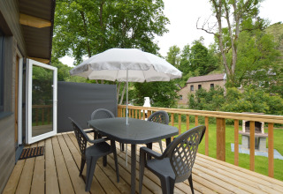 Terrasse im Le Chalet Chaleureux B, Belgien, mit Tisch, Stühlen, Sonnenschirm und grünem Ausblick.