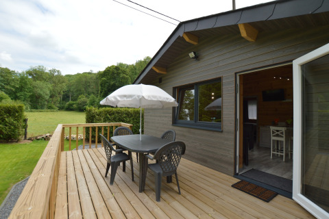 Holzterrasse mit Tisch, vier Stühlen und Sonnenschirm beim Le Chalet Chaleureux B, umgeben von Natur in Belgien.