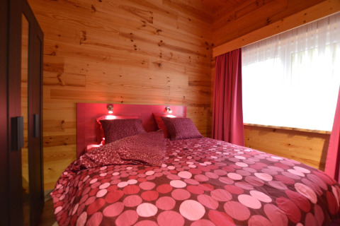 Schlafzimmer im Le Chalet Chaleureux B, Belgien, mit Holzdekor und pinkfarbener Bettwäsche.