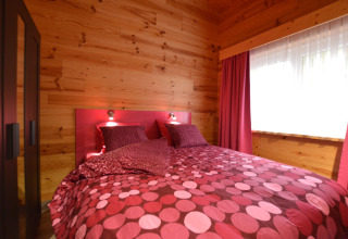 Schlafzimmer im Le Chalet Chaleureux B, Belgien, mit Holzdekor und pinkfarbener Bettwäsche.