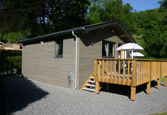 Außenansicht von Le Chalet Chaleureux B, einer Holzlodge mit Terrasse und Sonnenschirmen im Grünen.