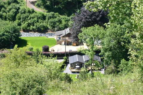 Blick auf Le Chalet Chaleureux B in Belgien, umgeben von üppigem Grün und Bäumen im Sommer