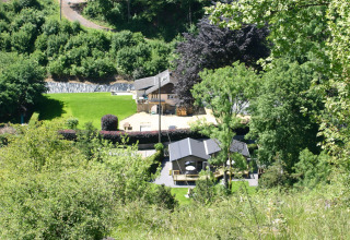 Blick auf Le Chalet Chaleureux B in Belgien, umgeben von üppigem Grün und Bäumen im Sommer