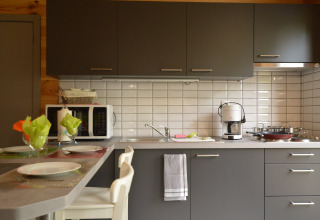 Moderne Küche in Le Chalet Chaleureux B, Belgien, mit grauen Schränken, Kaffeemaschine und Esstisch.