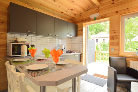 Moderne Küche mit Holzwänden, gedecktem Tisch, bunten Servietten und Zugang zur Terrasse in Belgien.