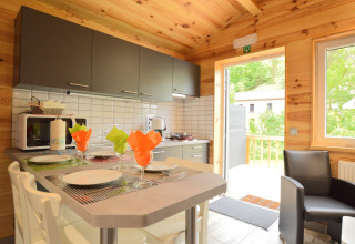 Moderne Küche mit Holzwänden, gedecktem Tisch, bunten Servietten und Zugang zur Terrasse in Belgien.