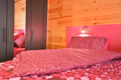 Schlafzimmer im Le Chalet Chaleureux B, Belgien, mit rosa Bettwäsche, Holzwänden und modernen Schränken.
