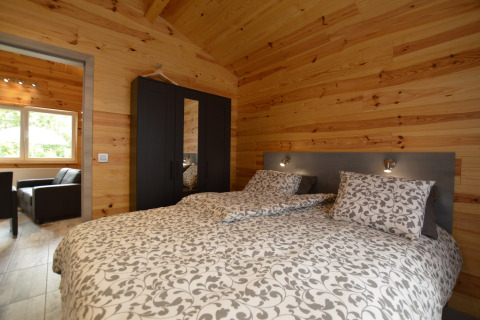 Gemütliches Schlafzimmer mit Doppelbett, Holzverkleidung und schwarzem Kleiderschrank im Le Chalet Chaleureux B, Belgien.