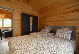 Gemütliches Schlafzimmer mit Doppelbett, Holzverkleidung und schwarzem Kleiderschrank im Le Chalet Chaleureux B, Belgien.