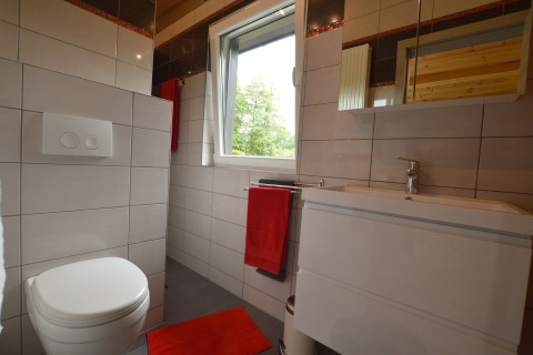 Modernes Badezimmer mit weißer Toilette, Waschbecken und roten Handtüchern im Le Chalet Chaleureux B in Belgien.