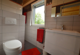 Modernes Badezimmer mit weißer Toilette, Waschbecken und roten Handtüchern im Le Chalet Chaleureux B in Belgien.