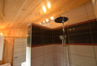 Moderne Duschkabine mit Holzdecke und Fliesen in einem Badezimmer von Le Chalet Chaleureux B in Belgien.