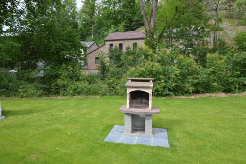Garten mit Rasen, gemauertem Grill und Haus im Hintergrund bei Le Chalet Chaleureux B, Belgien.