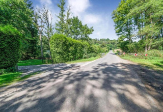Eine idyllische Landstraße umgeben von grünen Bäumen nahe Le Chalet Chaleureux B in Belgien bei Sonnenschein.
