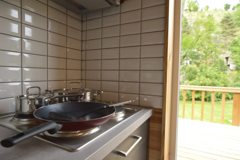 Moderne Küche mit Pfanne und Töpfen auf dem Herd, Blick auf grüne Terrasse im Le Chalet Chaleureux B, Belgien.