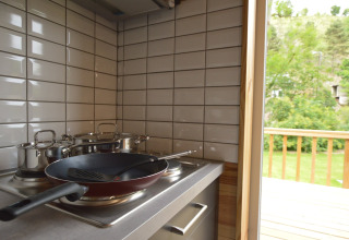 Moderne Küche mit Pfanne und Töpfen auf dem Herd, Blick auf grüne Terrasse im Le Chalet Chaleureux B, Belgien.