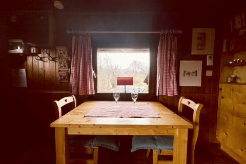 Tavolo di legno con due sedie e bicchieri vicino a una finestra nel chalet La Cabane, Belgio.
