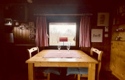 Træbord og to stole ved vindue med udsigt, røde gardiner, i en hyggelig chalet, La Cabane, Belgien.
