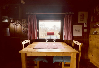 Tavolo di legno con due sedie e bicchieri vicino a una finestra nel chalet La Cabane, Belgio.