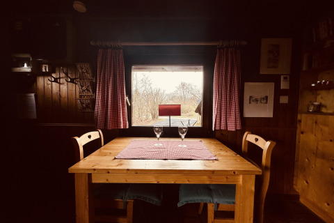 Houten tafel met twee stoelen en wijnglazen bij raam met rode gordijnen in chalet La Cabane, België.