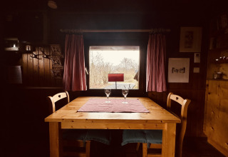 Houten tafel met twee stoelen en wijnglazen bij raam met rode gordijnen in chalet La Cabane, België.