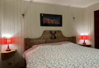 Camera da letto nello chalet 'La Cabane' in Belgio con letto matrimoniale, lampade rosse e pareti in legno.