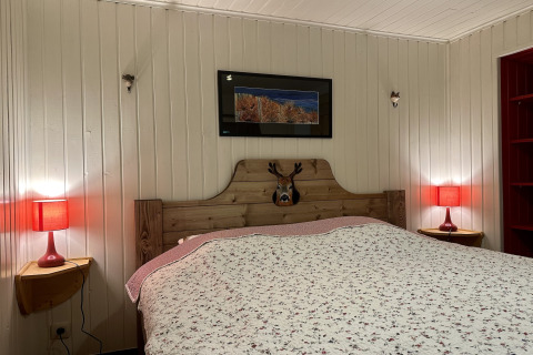 Slaapkamer in chalet 'La Cabane' in België met tweepersoonsbed, rode lampen en houten wandpanelen.