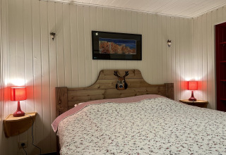 Slaapkamer in chalet 'La Cabane' in België met tweepersoonsbed, rode lampen en houten wandpanelen.