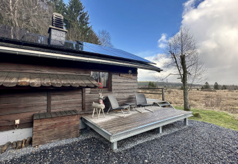 Træchaletet ‘La Cabane’ i Belgien med solpaneler, terrasse og udsigt over det omkringliggende landskab.