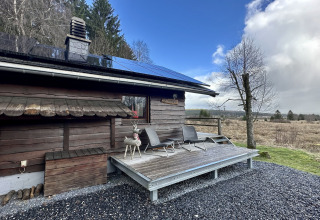 Chalet ‘La Cabane’ in België met zonnepanelen, houten terras en uitzicht op het landelijke landschap.