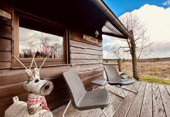 Træhytte kaldet 'La Cabane' i Belgien med to stole, træfigur af rensdyr og naturskønt landskab.
