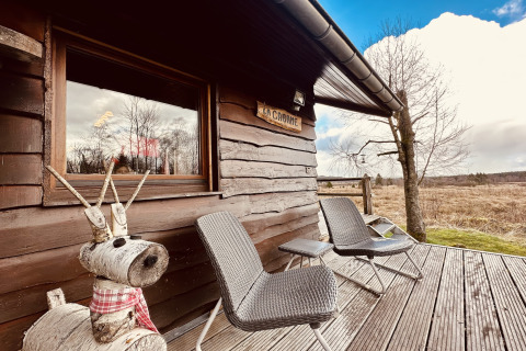 'La Cabane' chalet in België met twee stoelen, houten rendierbeeld en uitzicht op de natuur.